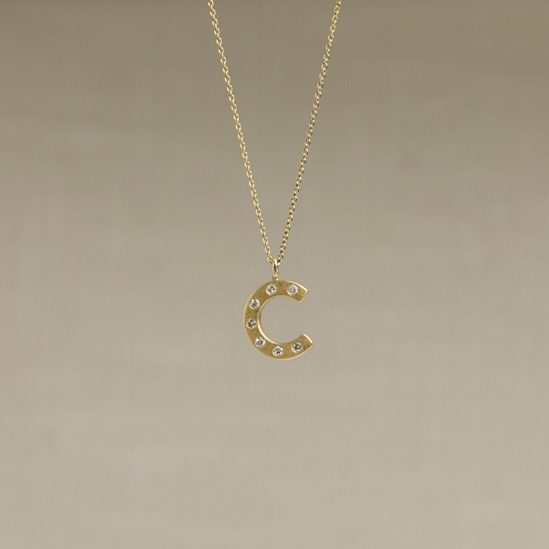 After — a gold initial pendant, stones flush-set
